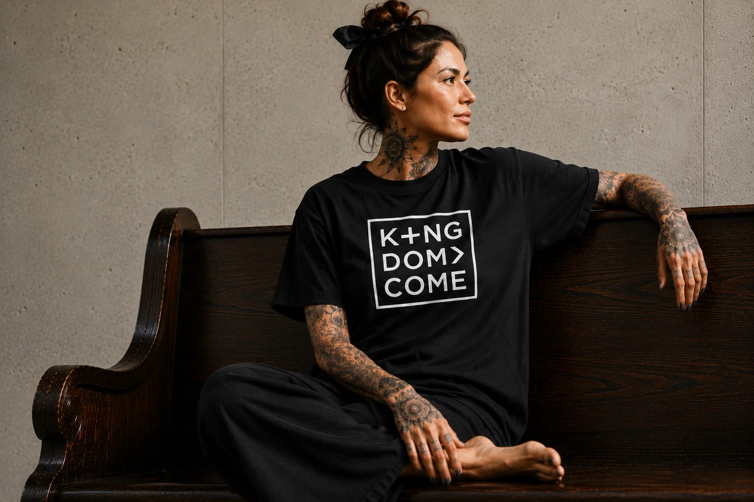 Woman seated on a church pew wearing the Kingdom Come tee