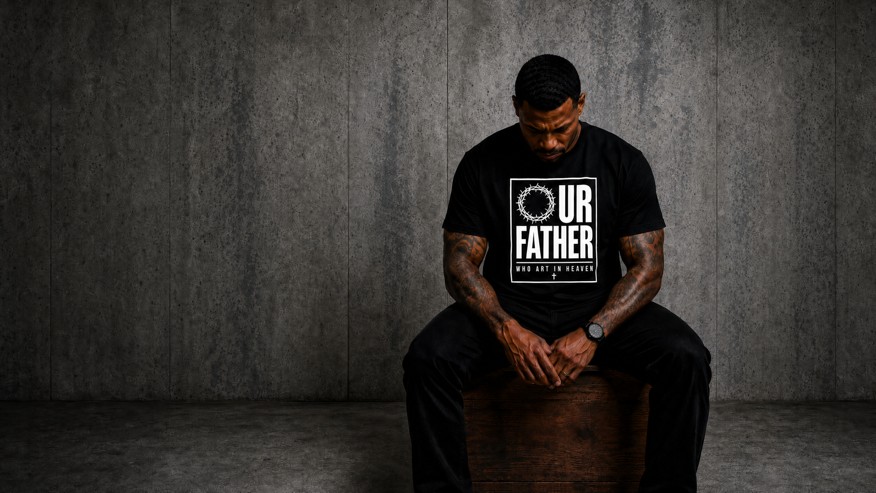 Man seated with hands clasped wearing the Our Father tee